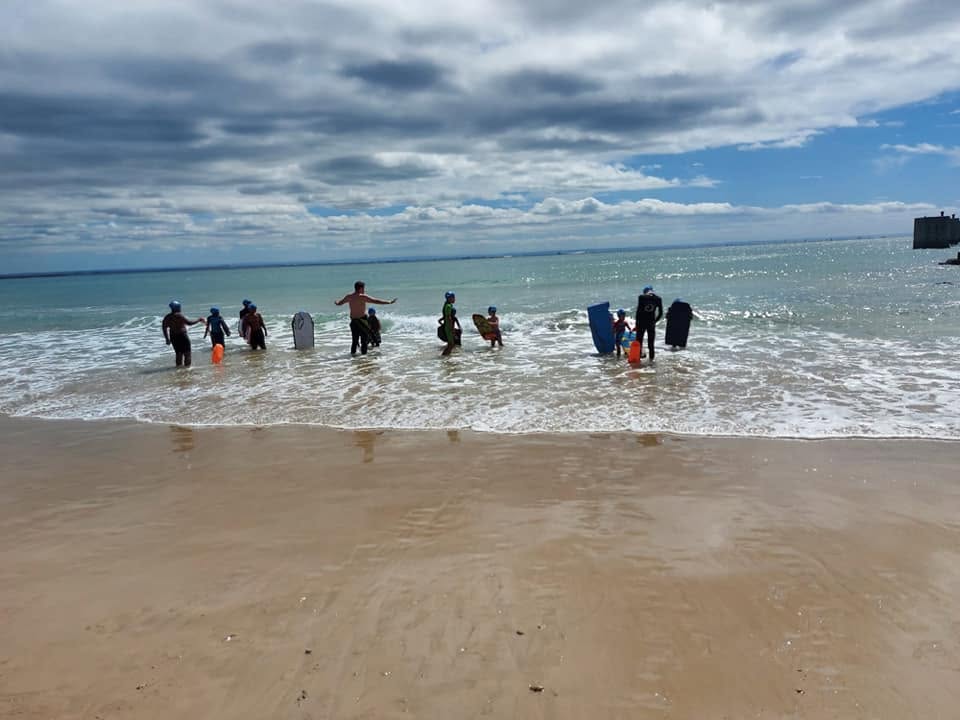Children with bodyboards heading into the surf with a Coastal Aquatics coach