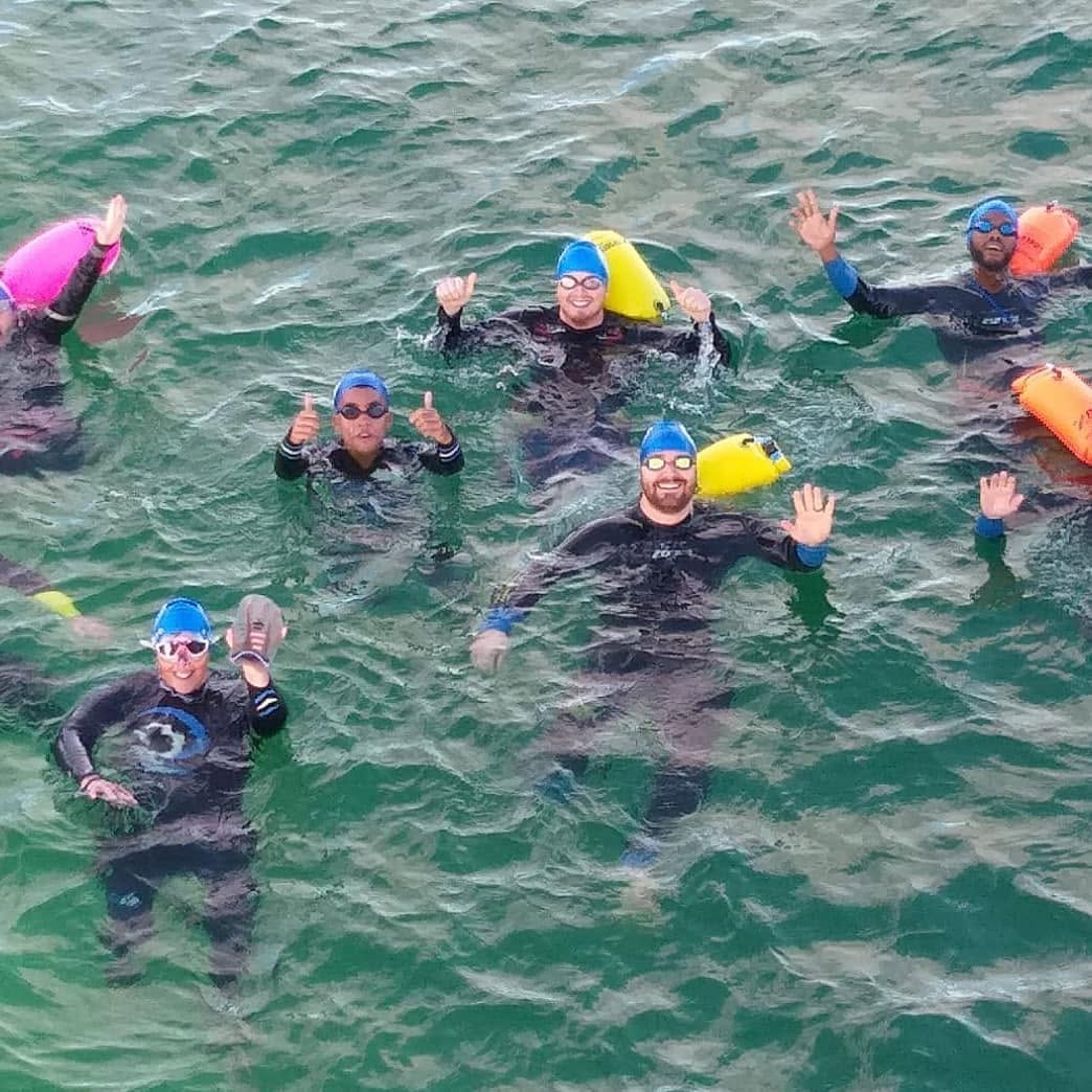 Open-water swimmers in caps and wetsuits during a Coastal Aquatics sea session